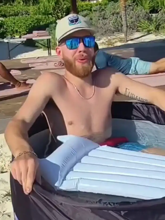 Un huésped sentado en la tina montada sobre la tarima de madera de un resort, con la arena y la vegetación atrás